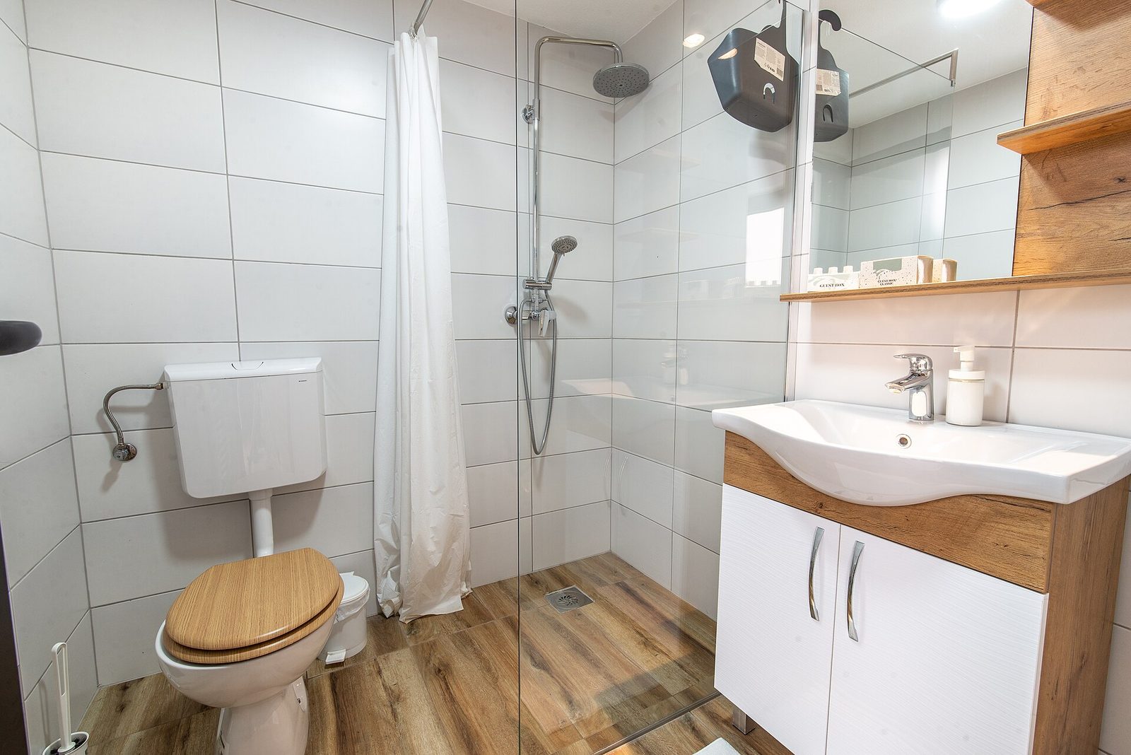 Kleine badkamer met inloopdouche achter een glazen wand, regendouche, houtlook vloertegels, toilet en wastafelmeubel