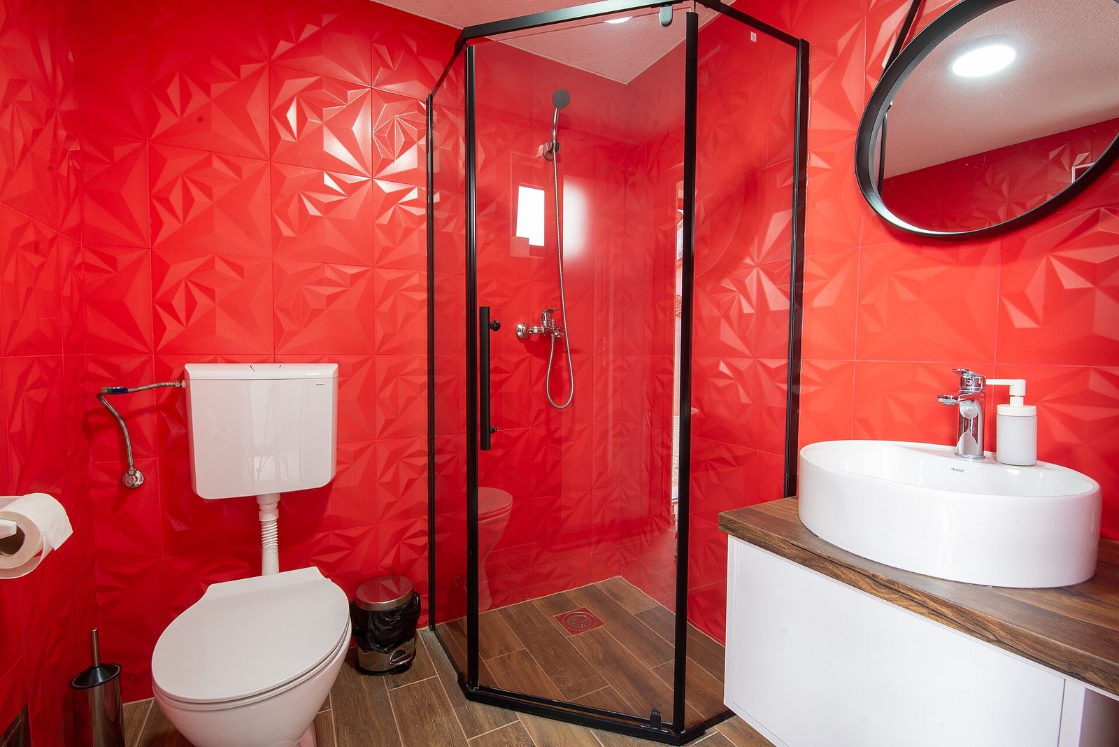 Moderne badkamer met een rode reliëfwand, glazen douchecabine, toilet met spoelbak aan de muur en een ronde wastafel
